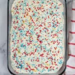 Top shot of jelo poke cake in a glass baking dish with a red and white stripped towel behind it.