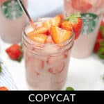Copycat Starbucks Pink Drink in a mason jar with a metal straw, garnished with fresh strawberry slices. In the background, a Starbucks cup brims with the same delicious drink.