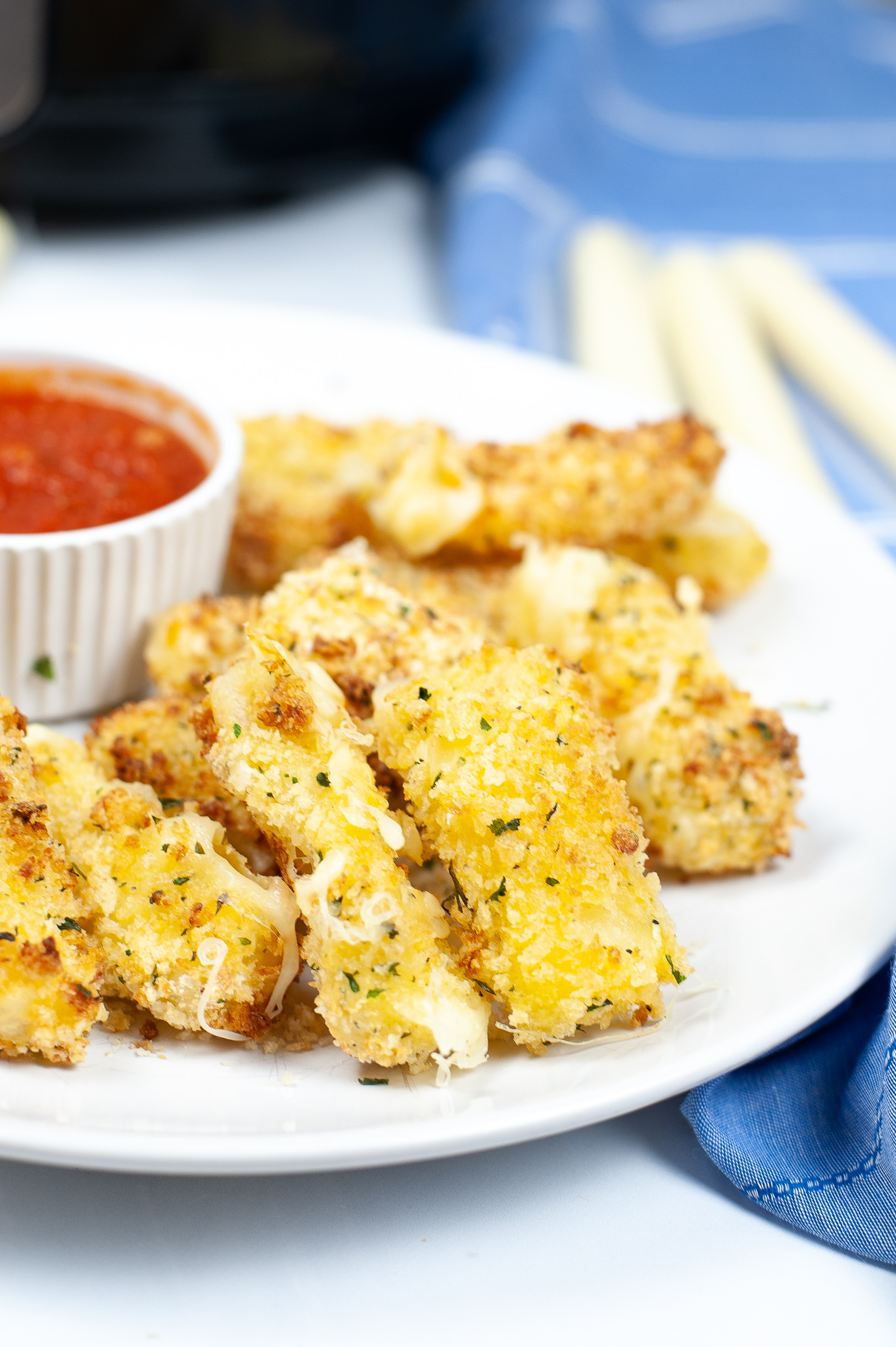 Plate of air fryer Mozzrella Sticks with a side of marinara sauce.