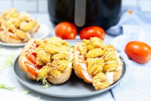 Two Shrimp Po Boy Sandwiches on a blue plate with an Air Fryer in the background.