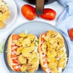 Finished Shrimp Po Boy Sandwiches on a blue plate with tomatoes and air fryer in the background.