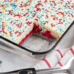 A rectangular glass dish with white frosting topped with red, blue, and yellow sprinkles.