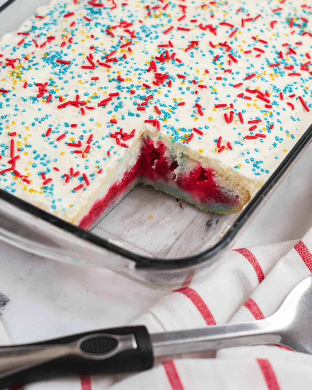 A rectangular glass dish with white frosting topped with red, blue, and yellow sprinkles. 