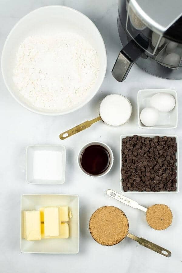 Baking ingredients arranged on a countertop for the perfect pizookie: flour, sugar, chocolate chips, brown sugar, butter, vanilla extract, eggs, and salt.