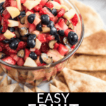 A glass bowl filled with a vibrant fruit salsa mix of strawberries, blueberries, and apples sits surrounded by sliced pita chips. Text at the bottom reads "Easy Fruit Salsa".