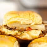 Close-up of a steak slider cheeseburger with a slice of onion, served on a bun.