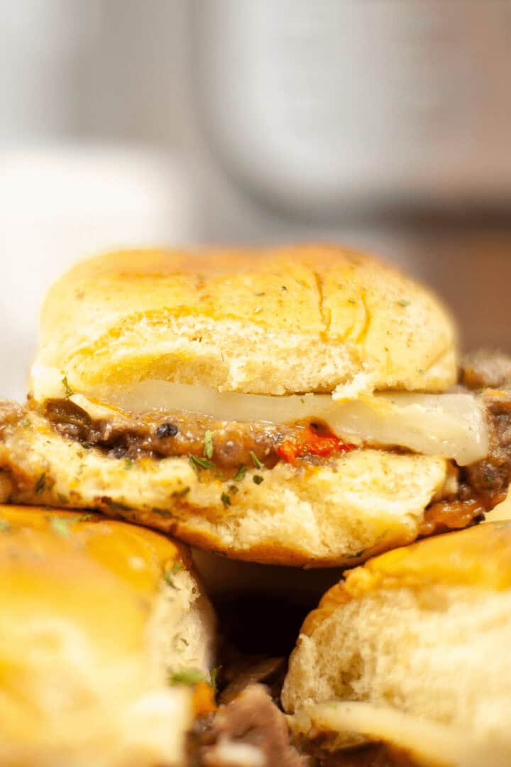 Close-up of a steak slider cheeseburger with a slice of onion, served on a bun.