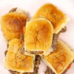 Five sliders with golden buns and fillings visible, reminiscent of a juicy steak slider experience, are perfectly arranged on a white plate.