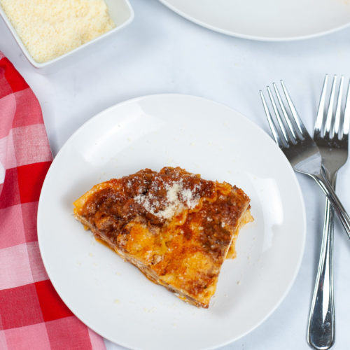 Slice of Instant Pot Lasagna on a round white dish with a fork and check napkin.