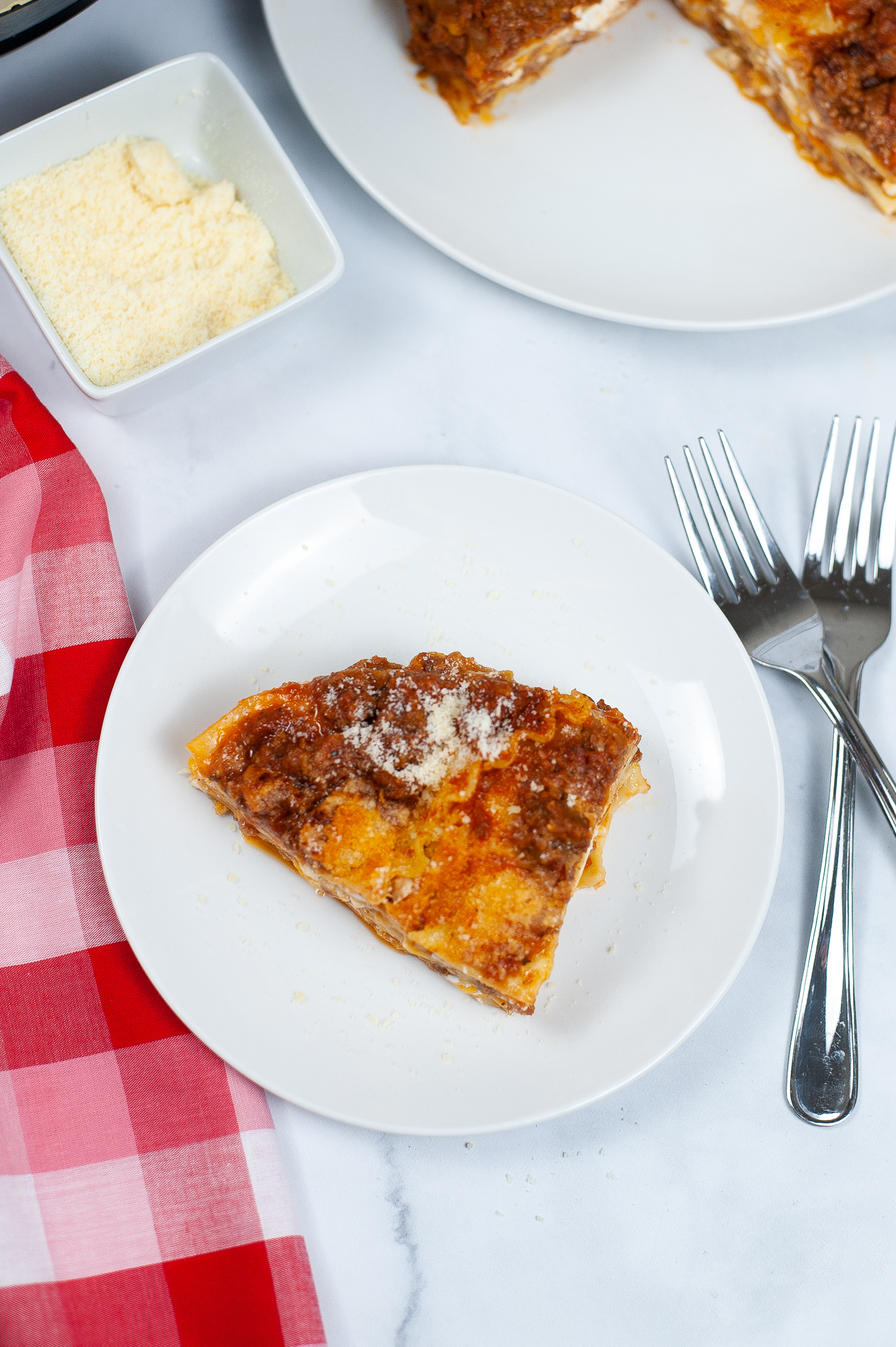 Slice of Instant Pot Lasagna on a round white dish with a fork and check napkin.