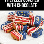 A plate of patriotic pretzels covered in chocolate, adorned with red, white, and blue decorations and topped with star-shaped sprinkles.