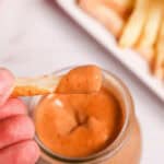 A hand holding the fry dipped into the sauce.