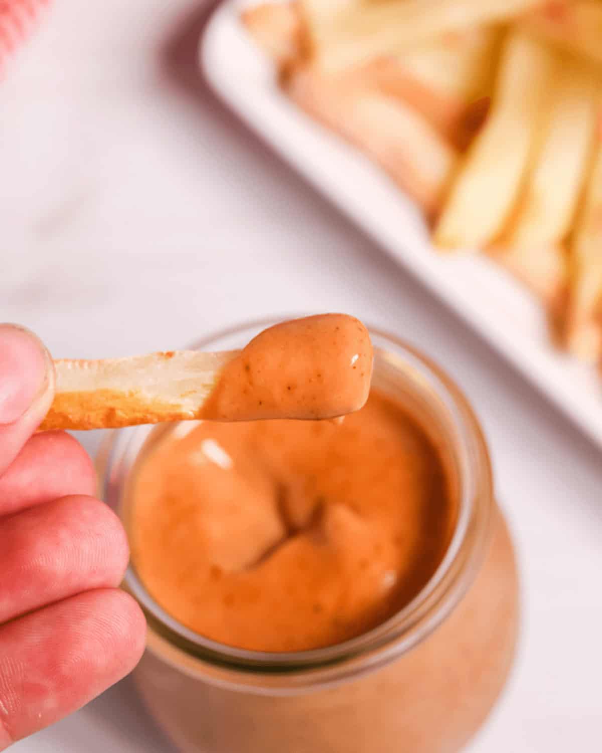 A hand holding the fry dipped into the sauce.