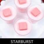 Close-up of five cups of Strawberry Jello Shots, each topped with a pink Starburst candy, displayed on a white tray. Text at the bottom reads "Starburst Strawberry Jello Shots".