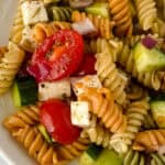 A close-up of a colorful Rotini Pasta Salad with rotini pasta, sliced cherry tomatoes, cubed cheese, cucumber pieces, red onions, and seasoning.