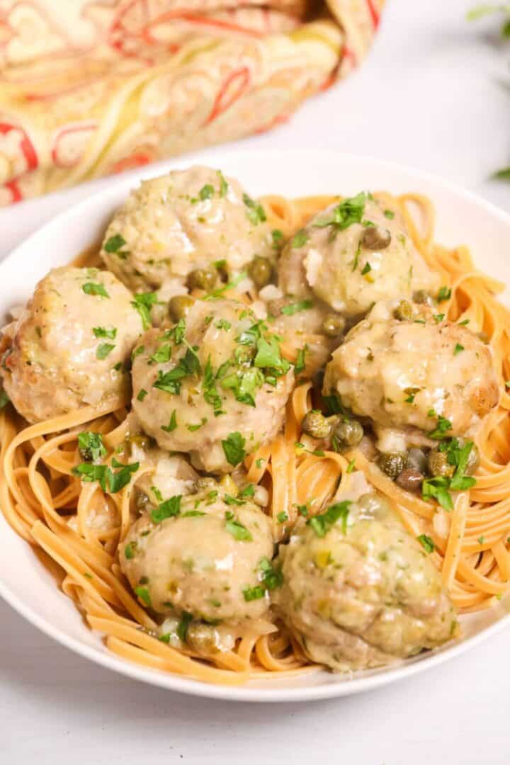 A white serving bowl with veal meatballs in piccata sauce.