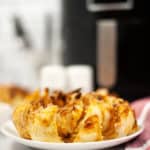 Side view of air fryer blooming onion on a white plate with air fryer and salt and pepper shakers in the background.