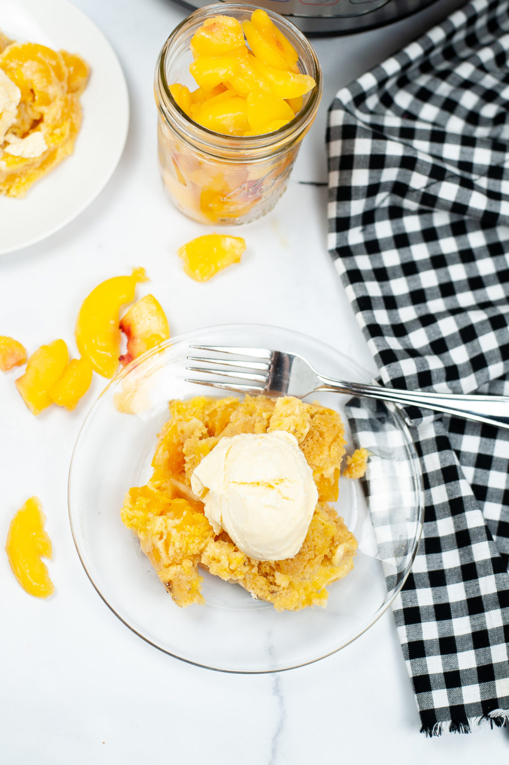 Instant Pot peach cobbler with peaches surrounding it and a fork on a clear plate.