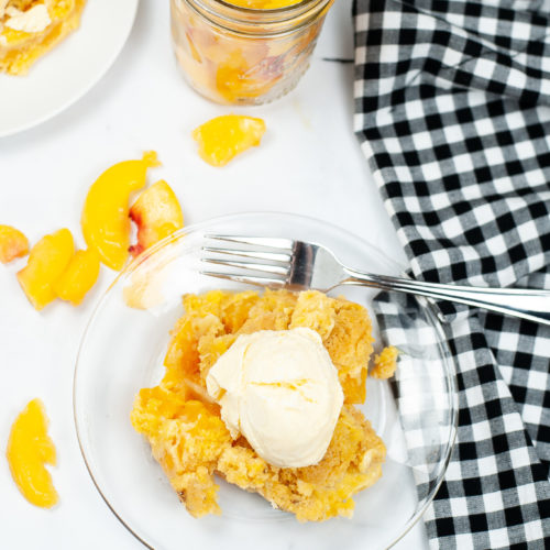 Instant Pot peach cobbler with peaches surrounding it and a fork on a clear plate.