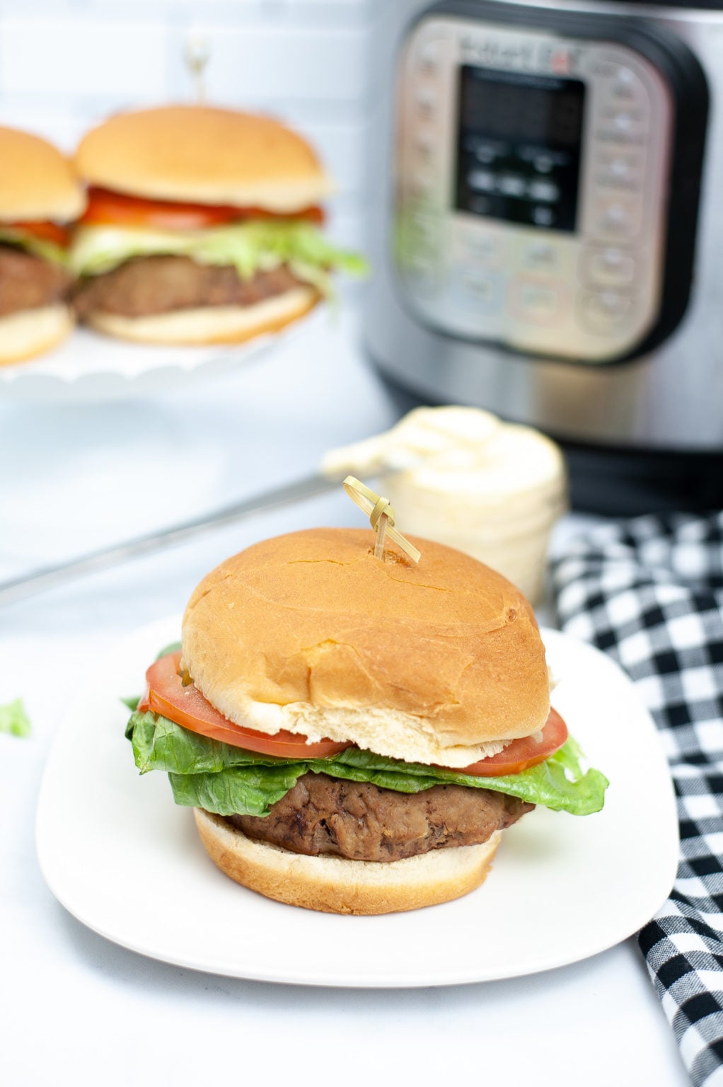 A picture of a turkey burger on a white plate with the instant pot in the background.