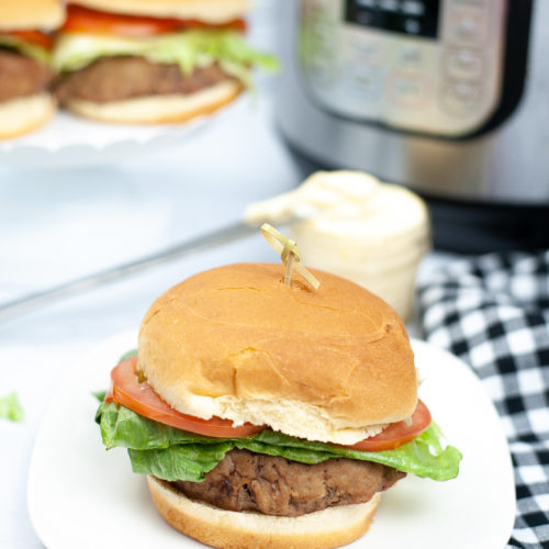 A picture of a turkey burger on a white plate with the instant pot in the background.