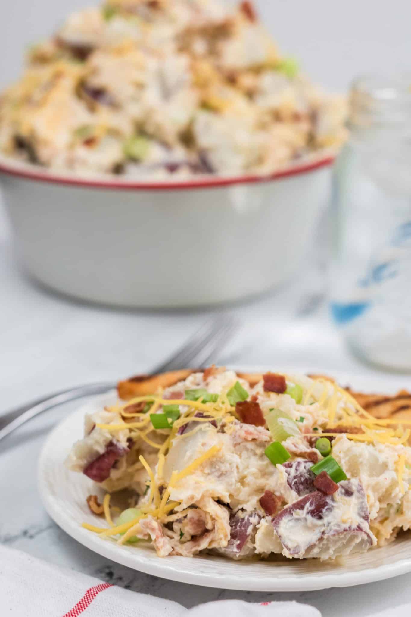 A dish of loaded baked potato salad with a big bowl of salad on the side.