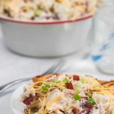 A dish of loaded baked potato salad with a big bowl of salad on the side.