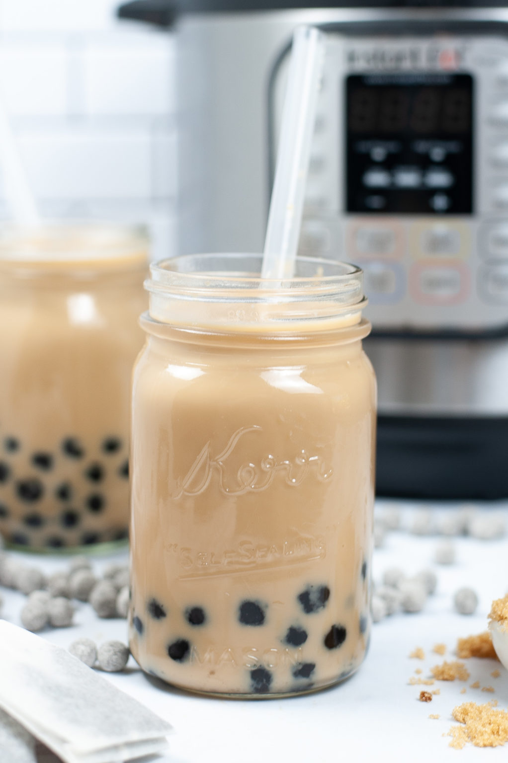 Mason Jar filled with Bubble Milk Tea with a white straw init, with back tapioca bubbles around it.