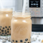 Mason Jar filled with Bubble Milk Tea with a white straw init, with back tapioca bubbles around it.