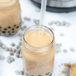 Shot of Milk Tea with a straw in it and a scattering of the tapioca pearls beside it.