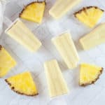 Slices of pineapple surround pina colada popsicles.