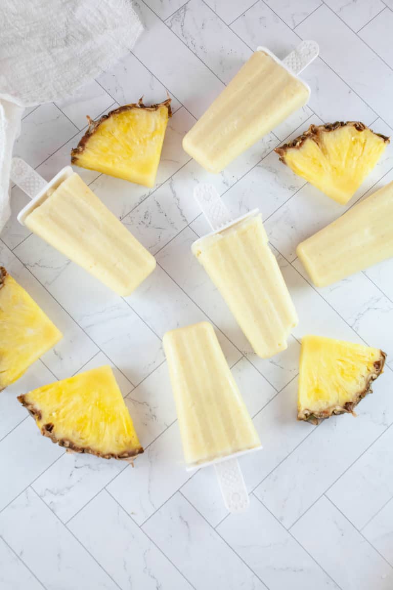 Slices of pineapple surround pina colada popsicles.