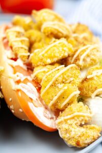 A classic meal, packed with fried shrimp, crisp lettuce, and juicy tomato, all drizzled with a tangy yellow sauce and served in a fresh hoagie roll.