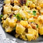 A close-up of a cheesy potato casserole with chopped herbs, served on a decorative gray plate—perfect for a hearty Cast Iron Skillet Breakfast.