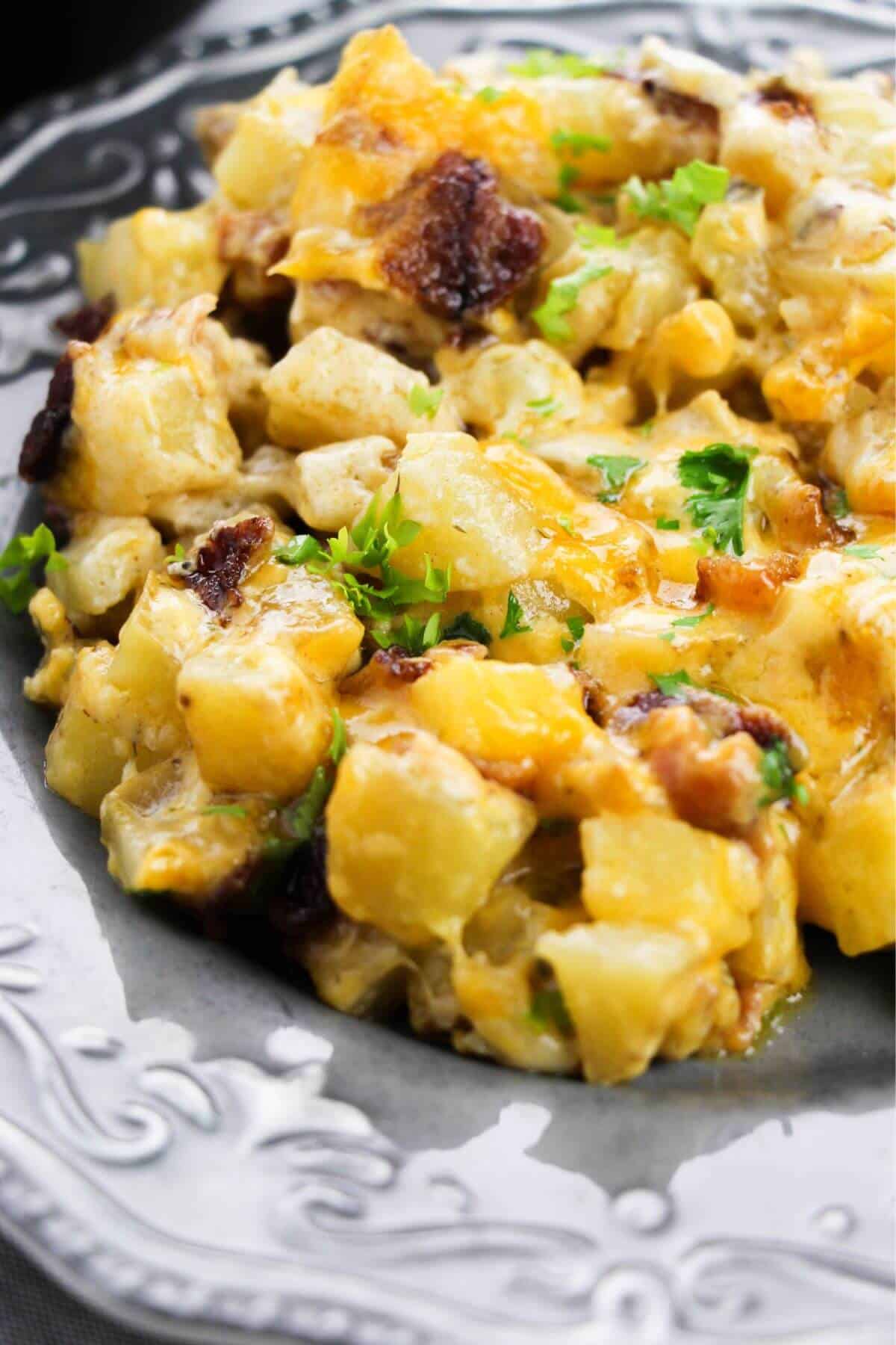 A close-up of a cheesy potato casserole with chopped herbs, served on a decorative gray plate—perfect for a hearty Cast Iron Skillet Breakfast.