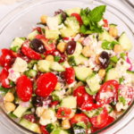 A fresh Chickpea Feta Salad with cucumbers, tomatoes, red onions, olives, and feta cheese in a glass bowl.