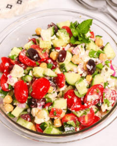 A fresh Chickpea Feta Salad with cucumbers, tomatoes, red onions, olives, and feta cheese in a glass bowl.