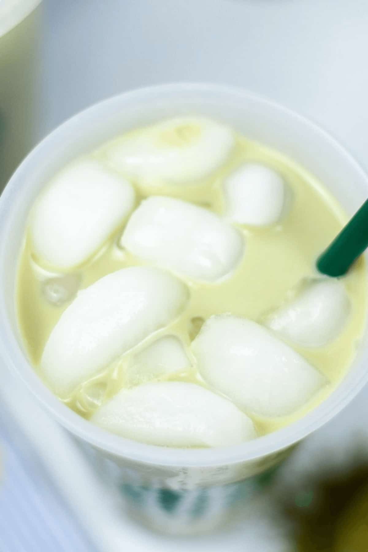 A cup of iced matcha latte with a green straw, filled with ice cubes, offers a creamy yellow delight.