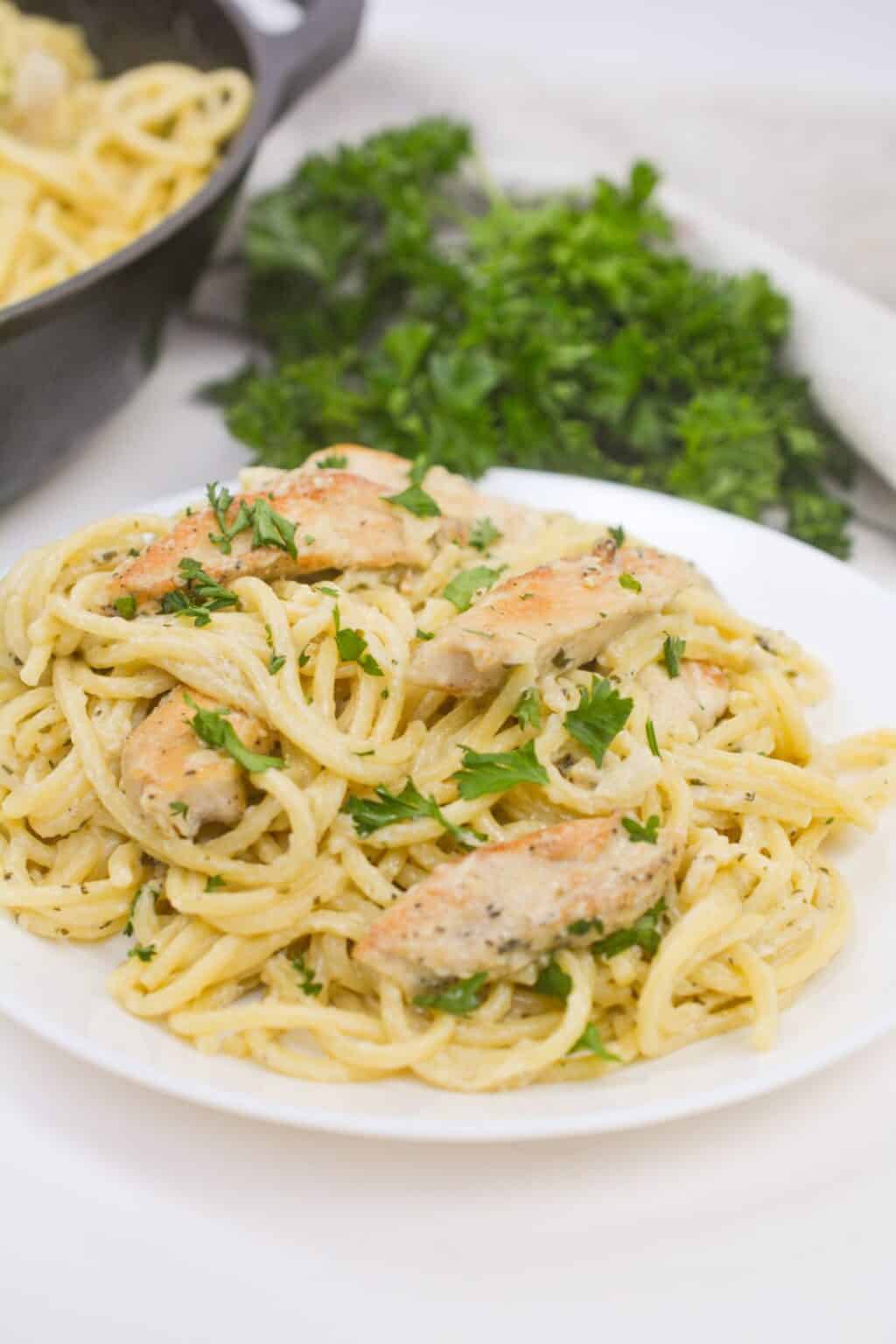 A plate of dinner garnished with chopped parsley, sits on a white plate with fresh parsley in the background.