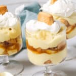 Three glass dishes of layered, dessert topped with whipped cream and a cookie, next to a blue napkin and a gold spoon.