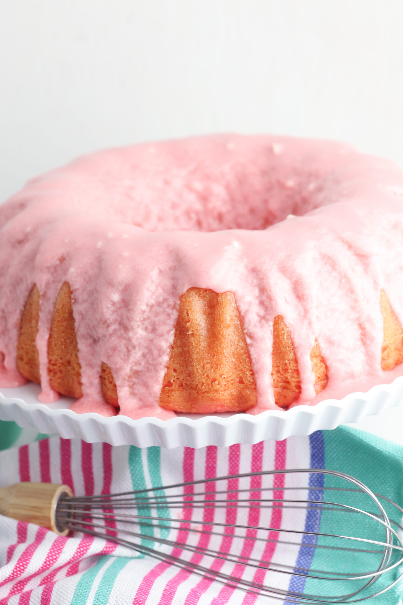 A blue and pink stripped napkin with a cake stand on it with a cherry limeade cake in the bundt style.