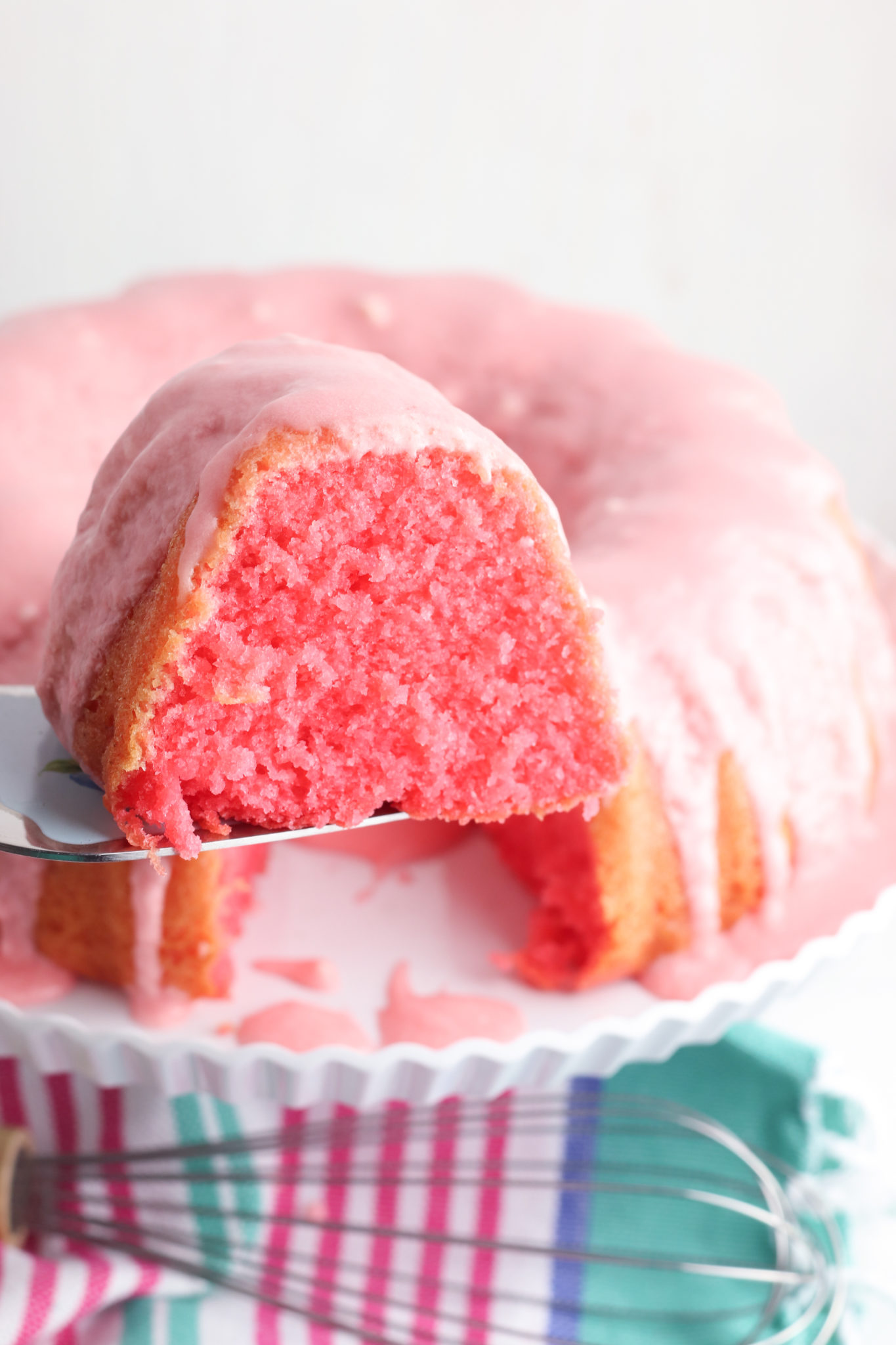 Slice of cherry limeade cake on a server with the remaining cake in the background.