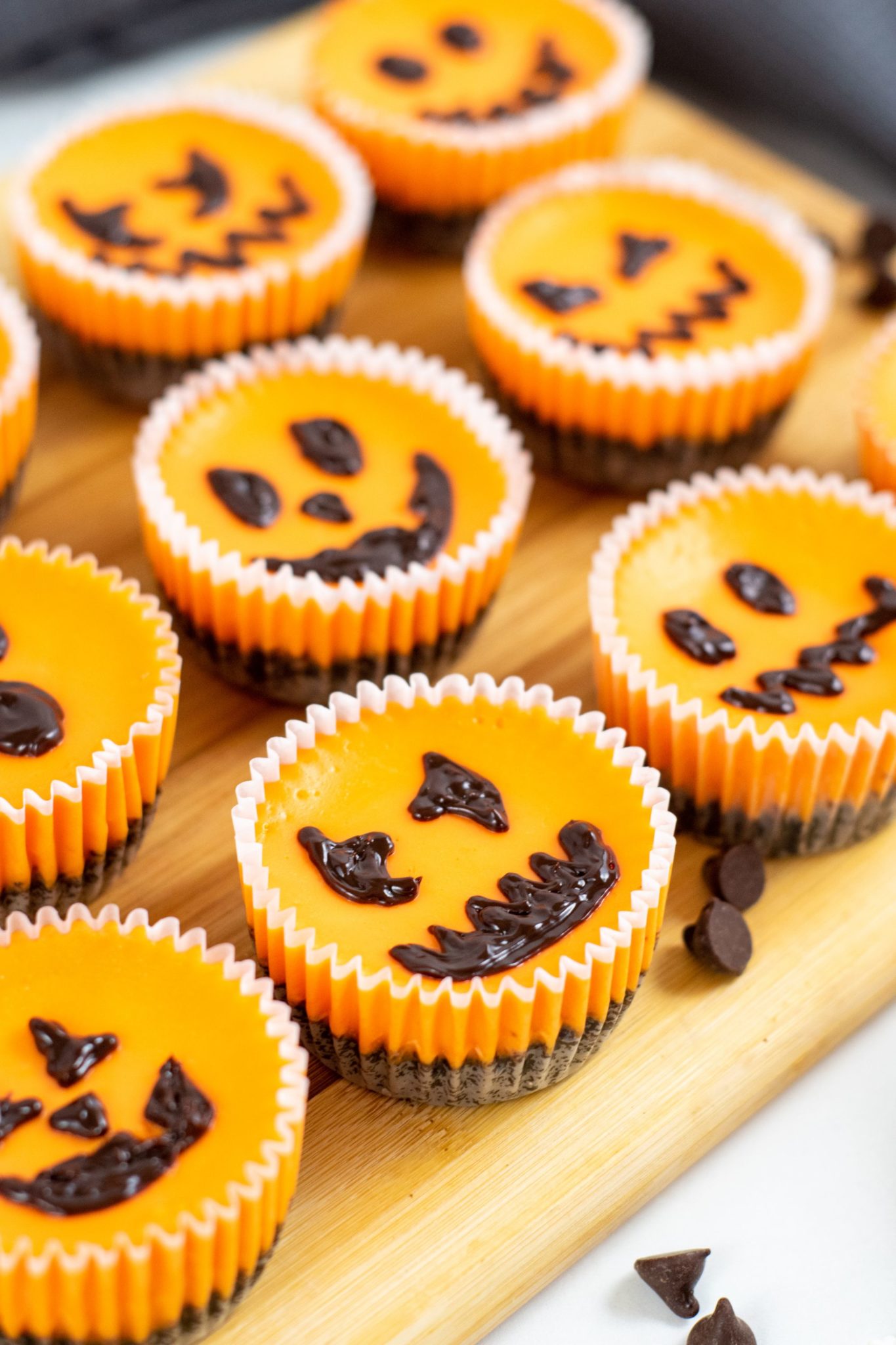 Cutting board filled with mini Halloween cheesecakes with all different faces.