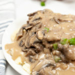 Close up of salisbury steak on a white late with mushrooms and gravy.