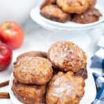 White dish of apple fritters with apples in the background.