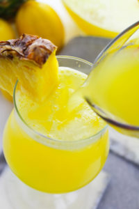 Side view of a glass of pineapple lemonade with a piece of pineapple on the glass.