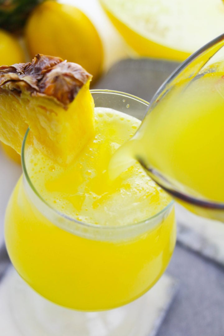 Side view of a glass of pineapple lemonade with a piece of pineapple on the glass.