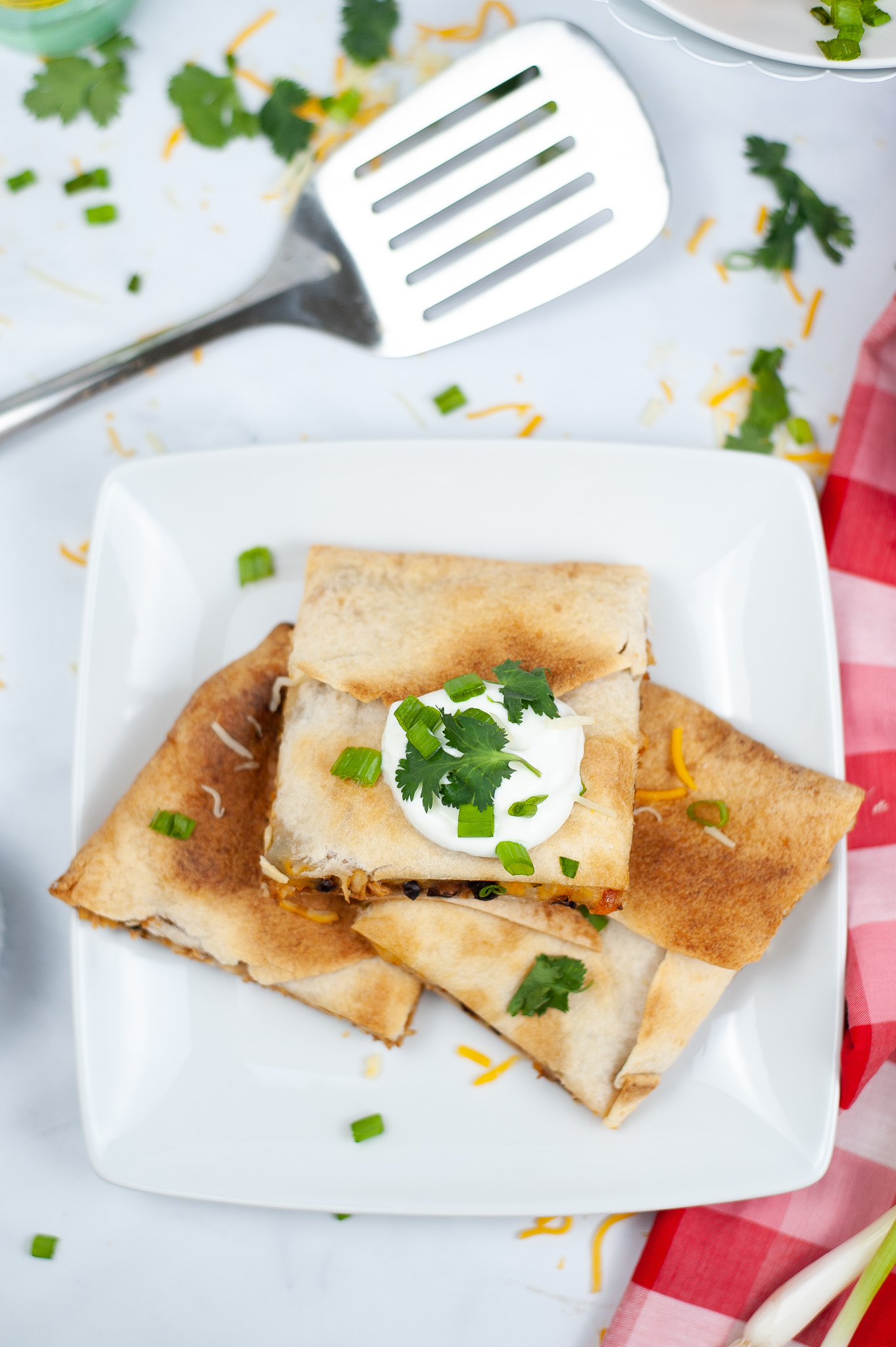 Shredded Chicken Quesadilla Melt on a white square plate topped with sour cream and cilantro.