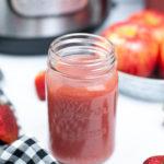 Masjon jar filled with strawberry applesauce with a black and white check napkin.