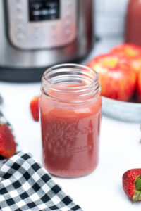 Masjon jar filled with strawberry applesauce with a black and white check napkin.